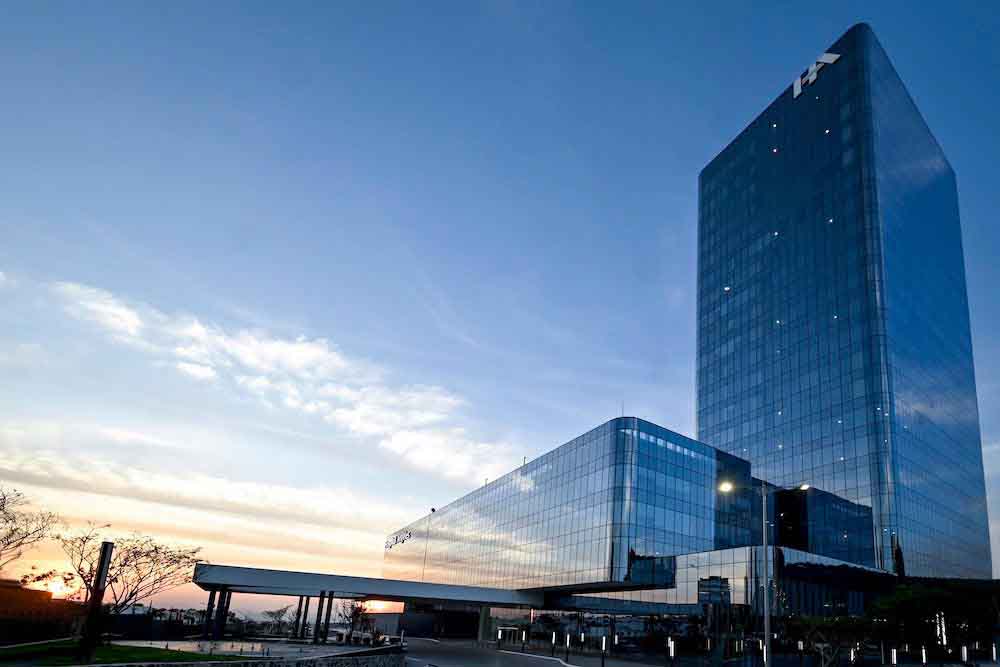 Edificio de cristal azul de 22 pisos y el atardecer de fondo.